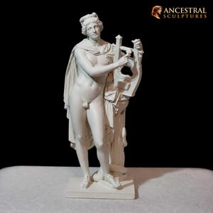 May include: A white sculpture of a nude male figure holding a lyre. The figure has a draped cloth over his shoulder and stands on a rectangular base. The sculpture is set against a black background. The text "ANCESTRAL SCULPTURES" is in the upper right corner.