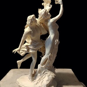 Peut inclure: Une sculpture en céramique blanche représentant deux figures, un homme et une femme, enlacés. La femme tend la main vers une branche de feuilles, tandis que l'homme la serre contre lui. La sculpture est posée sur une base blanche.