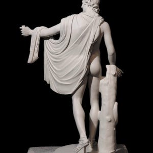 May include: A white plaster sculpture of a nude male figure standing with a drapery draped over his left arm. The figure is holding a small object in his right hand and is leaning against a tree trunk.