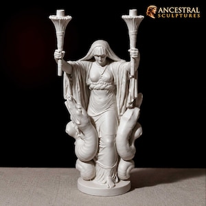 Puede incluir: Una escultura blanca que representa una figura vestida con un velo, sosteniendo una antorcha en cada mano levantada. La figura está flanqueada por dos grandes serpientes enroscadas que se elevan desde la base. El texto ANCESTRAL SCULPTURES es visible.
