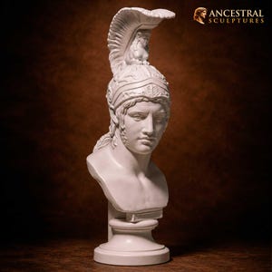Puede incluir: Un busto escultórico blanco de una figura que lleva un casco ornamentado con una cresta alta y una figura de esfinge en la parte superior. La escultura presenta rasgos faciales detallados, cabello ondulado y descansa sobre una base circular. El texto Ancestral Sculptures es visible.