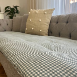 May include: A gray sofa with a light green and white gingham patterned cushion. The sofa has a tufted back and is upholstered in a light gray fabric.