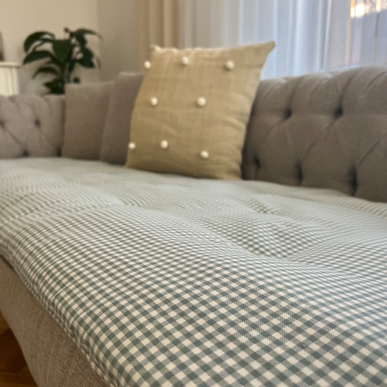 May include: A gray sofa with a light green and white gingham patterned cushion. The sofa has a tufted back and is upholstered in a light gray fabric.