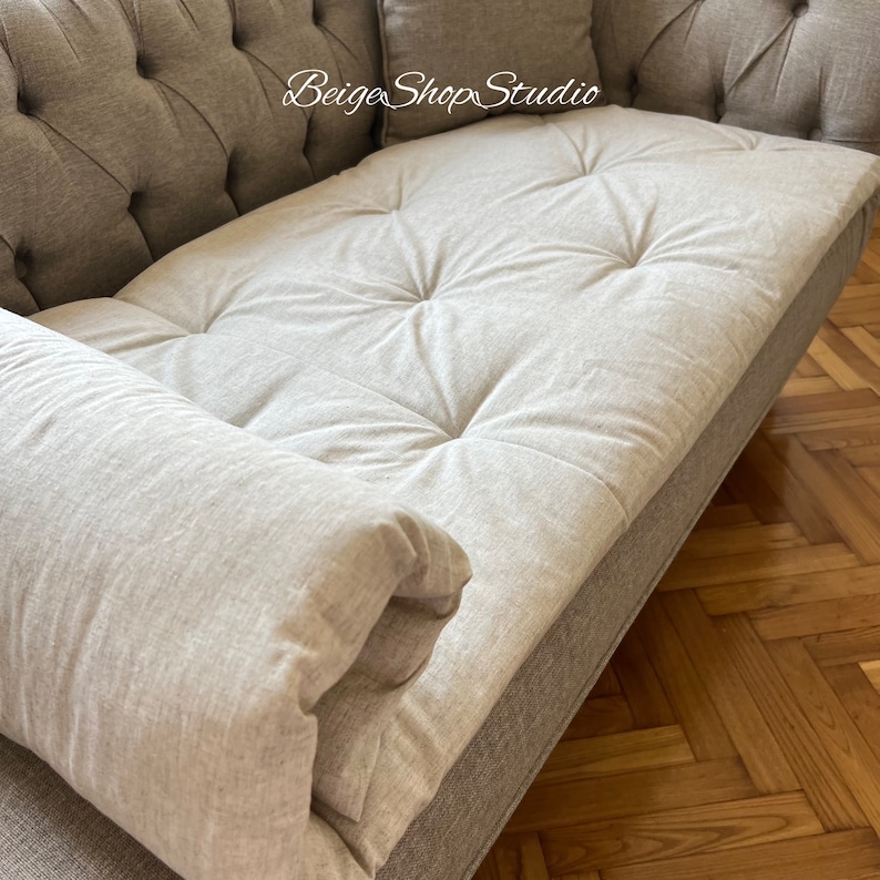 May include: A light gray tufted sofa with a light gray pillow. The sofa is made of a soft, textured fabric and has a classic design.