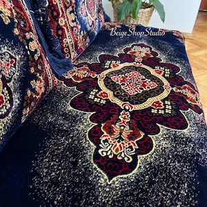 May include: A navy blue throw pillow with a gold, red, and white floral pattern. The pillow has a fringe border and is made of a soft, plush fabric.