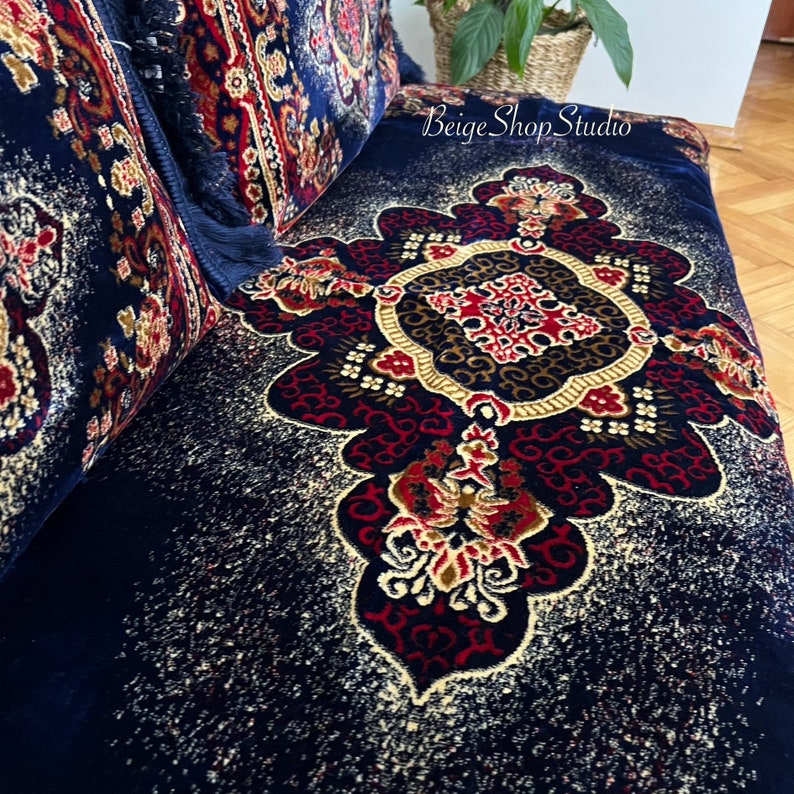 May include: A navy blue throw pillow with a gold, red, and white floral pattern. The pillow has a fringe border and is made of a soft, plush fabric.