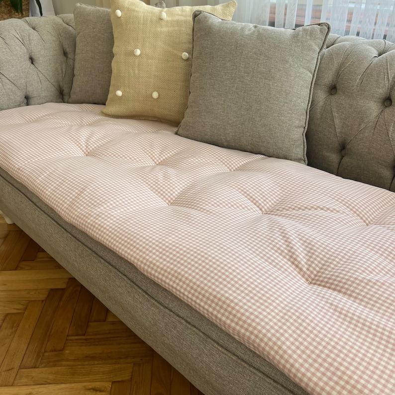 May include: A gray sofa with a pink and white gingham patterned cushion. The sofa has a tufted back and is upholstered in a gray fabric.
