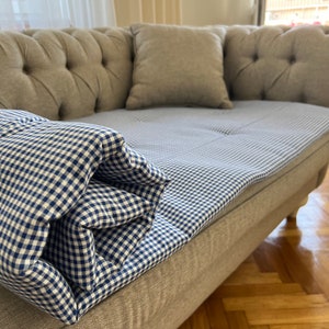 May include: A gray tufted sofa with a blue and white gingham patterned throw blanket on top. The sofa has two pillows, one on each end.