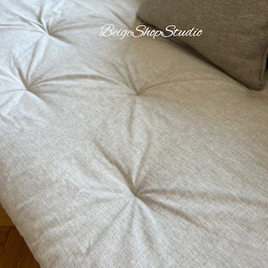 May include: Close-up of a light gray tufted fabric sofa cushion. The fabric has a subtle woven texture.