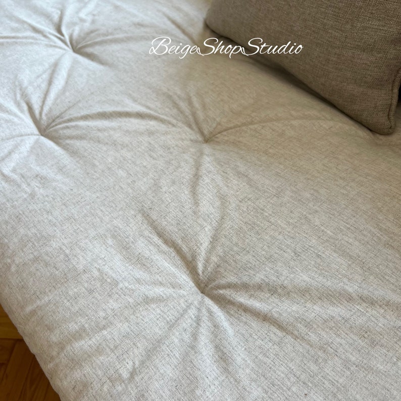 May include: Close-up of a light gray tufted fabric sofa cushion. The fabric has a subtle woven texture.