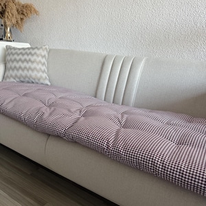 Może przedstawiać: Jasnoszara sofa z bordowo-białą poduszką w kratę. Na sofie spoczywa poduszka w paski. Poduszka jest pikowana guzikami. Suche trawy ozdobne znajdują się w wazonie po lewej stronie.