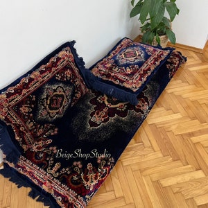 May include: A navy blue floor cushion with a red and gold patterned design. The cushion has fringe trim and is topped with two matching pillows.