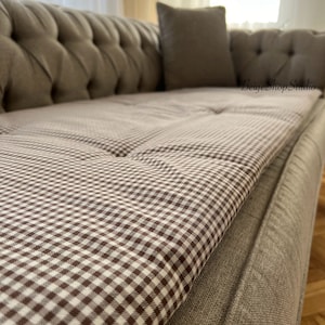 May include: A brown and white checkered sofa cushion with a brown sofa in the background.