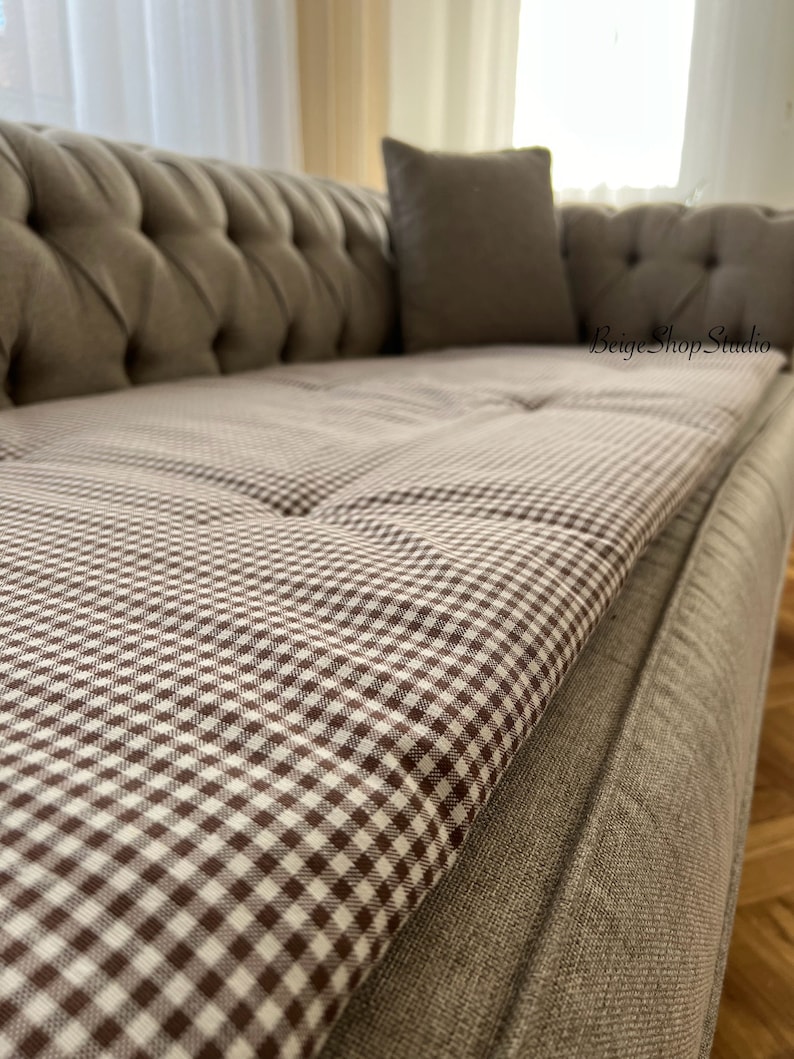 May include: A brown and white checkered sofa cushion with a brown sofa in the background.