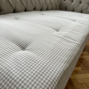 May include: A close-up of a gray tufted sofa with a white and gray gingham patterned cushion.