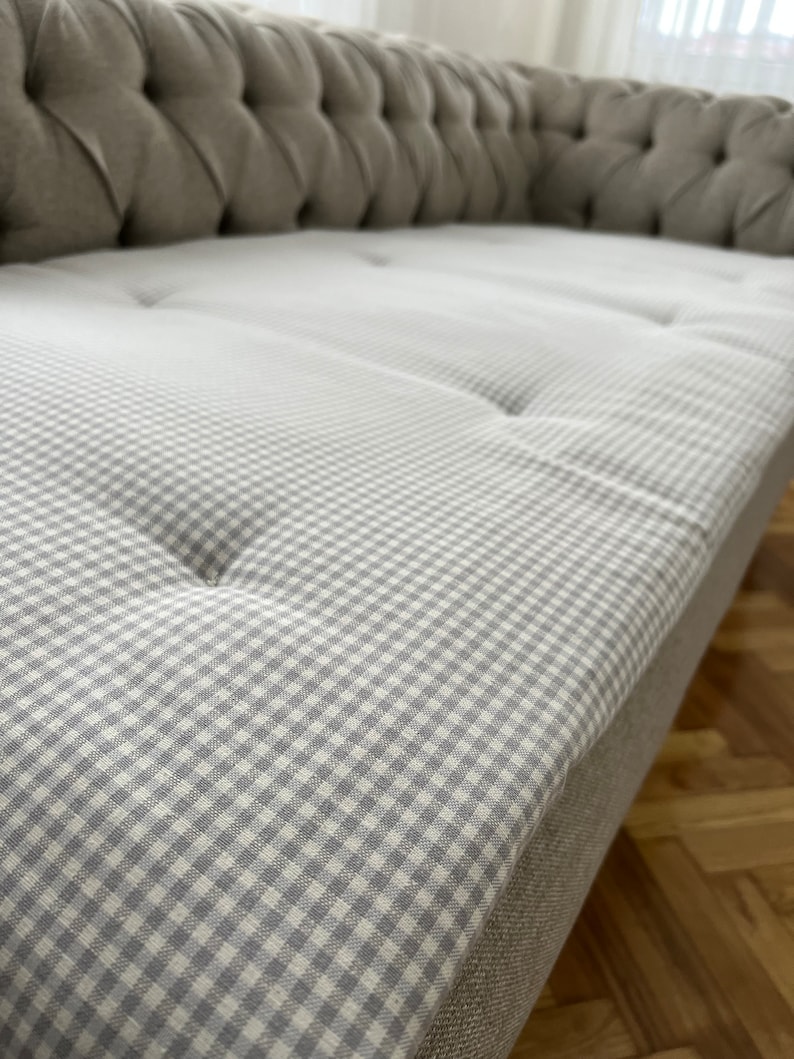 May include: A close-up of a gray tufted sofa with a white and gray gingham patterned cushion.