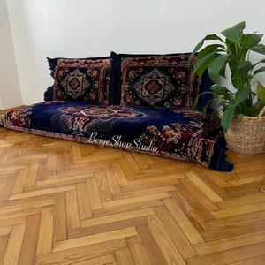 May include: A blue and red patterned floor cushion with two matching pillows. The cushion is on a wooden floor with a herringbone pattern.