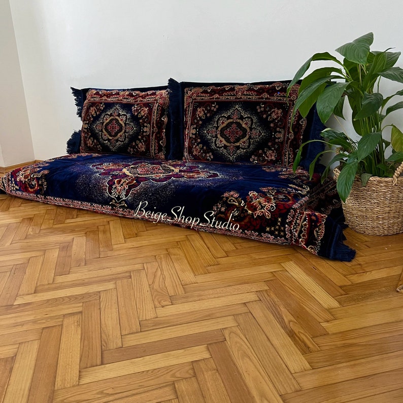 May include: A blue and red patterned floor cushion with two matching pillows. The cushion is on a wooden floor with a herringbone pattern.