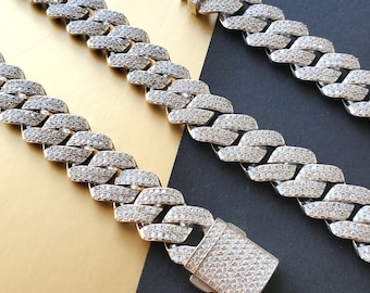 May include: A silver-coloured Cuban link chain necklace with a matching clasp, encrusted with small, clear stones. The chain's design creates a sparkling effect. The background is split between gold and black.