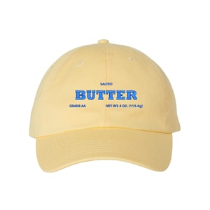 May include: A yellow baseball cap with the text "SALTED BUTTER" in blue lettering. The cap also has the text "GRADE AA" and "NET WT 4 OZ (113.4g)" in black lettering.