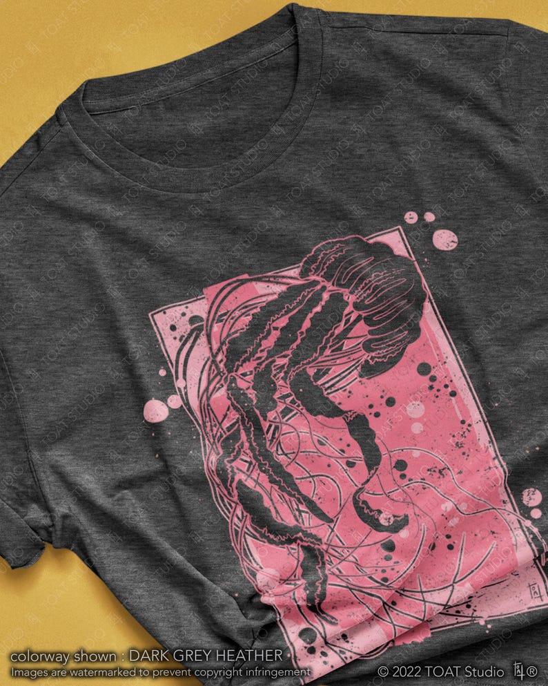 May include: A dark grey heather t-shirt with a pink and black graphic print of a jellyfish. The jellyfish is surrounded by pink splatter paint.