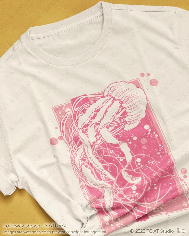 May include: A white t-shirt with a pink jellyfish graphic. The jellyfish is outlined in white and has a pink background. The graphic is surrounded by a pink square with white dots.