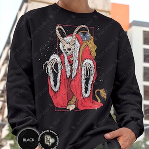 May include: Black sweatshirt featuring a red and white illustration of a horned skeletal figure in a red robe with white fur trim. The figure holds a sack and has a tail. The sweatshirt has the word "BLACK" printed on it.