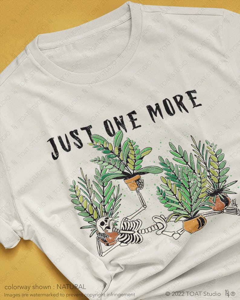 May include: A white t-shirt featuring the text "JUST ONE MORE" above a graphic of a skeleton tending to potted plants. The skeleton is surrounded by green plants in brown pots. The shirt is a natural color.