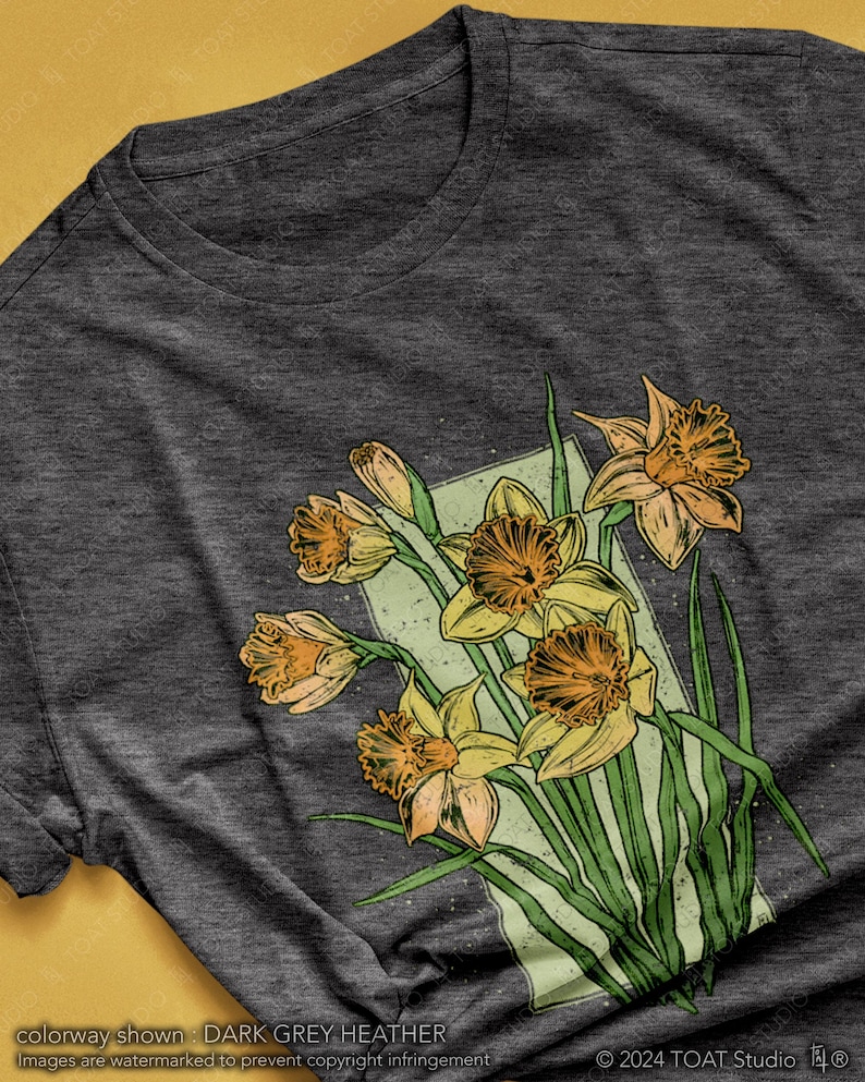 May include: A dark grey heather t-shirt with a graphic print of a bouquet of yellow daffodils with green leaves. The daffodils are drawn in a vintage style with a light green background.