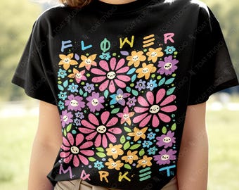 May include: Black t-shirt with a colorful floral design. The graphic features smiling flowers in pink, purple, yellow, and blue, with the words "FLOWER MARKET" in rainbow colors. The shirt is a casual, short-sleeved style.