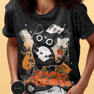 May include: Black t-shirt featuring a Halloween-themed graphic. The design includes a black cat with stitched details, a skull, pumpkins, and Japanese text. The shirt has a crew neck and short sleeves.