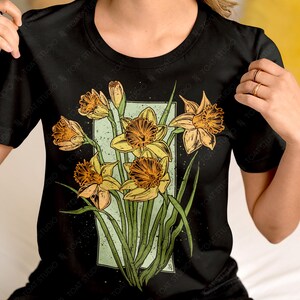 May include: Black t-shirt with a graphic print of a bouquet of yellow daffodils with green stems and leaves. The graphic is framed in a light blue rectangle.