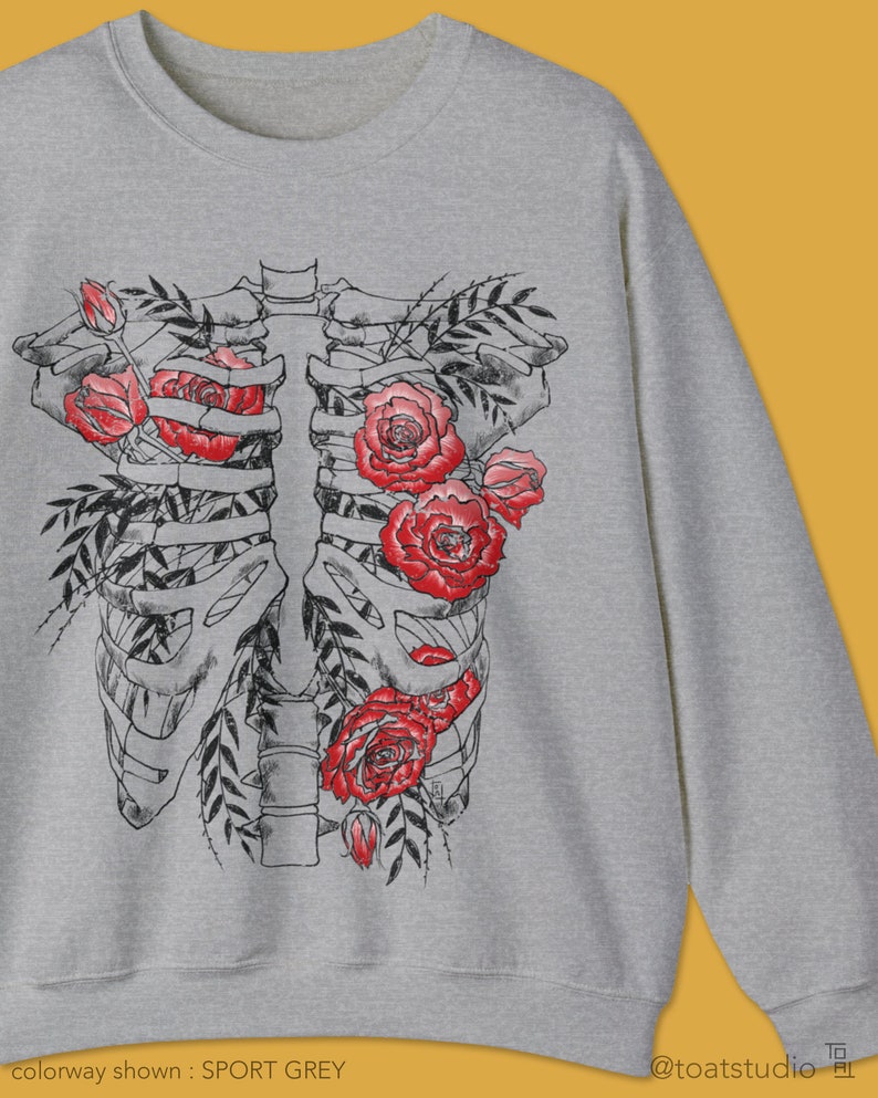 Pu&ograve; includere: Felpa grigio sport con un design a gabbia toracica floreale nera e rossa. La grafica include rose rosse e foglie nere. Il testo "colorway shown: SPORT GREY" &egrave; in basso nell'immagine, insieme al logo @toatstudio.