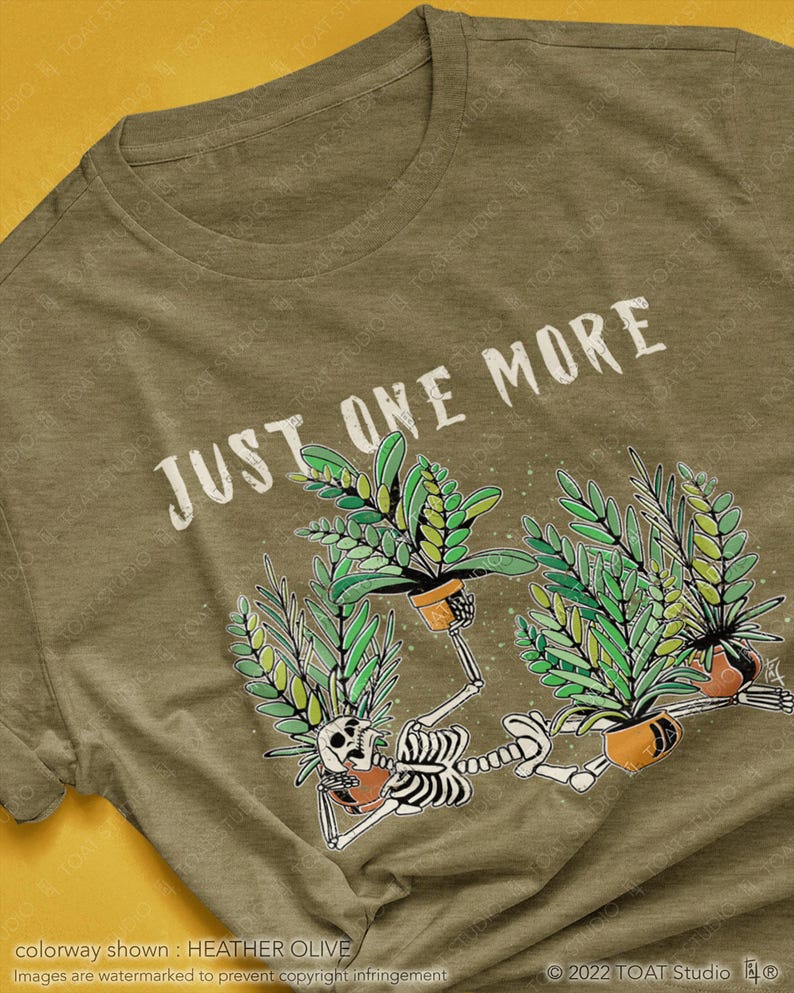 May include: Heather olive green t-shirt with the text "JUST ONE MORE" in white. The graphic features skeleton figures holding potted plants with green leaves. The shirt is a crew neck style.