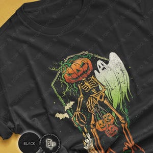 May include: Black t-shirt featuring a Halloween-themed graphic. The design includes a skeleton with a pumpkin head, a ghost, and bats. The color palette consists of orange, green, and white against a black background. The shirt is a crew neck.