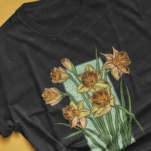 May include: A black t-shirt with a vintage-style illustration of a bouquet of yellow daffodils on a dark background.