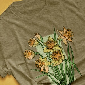 May include: A heather olive t-shirt with a vintage-style illustration of a bouquet of yellow daffodils with green leaves.
