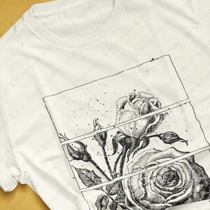 May include: A white t-shirt featuring a detailed black and white rose illustration within a rectangular frame. The design includes a large open rose, buds, and leaves. The shirt's colorway is natural.
