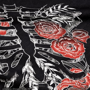 Pu&ograve; includere: Tessuto nero con un disegno di gabbia toracica scheletrica bianca, rose rosse e accenti di foglie. Il testo "colorway shown : BLACK" &egrave; in basso a sinistra. Il nome dell'artista, "@toatstudio", &egrave; in basso a destra.