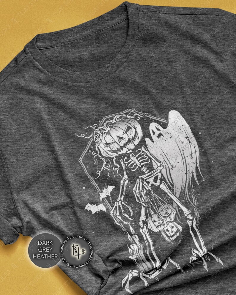 May include: Dark grey heather t-shirt featuring a white Halloween design. The graphic includes a skeleton with a pumpkin head, a ghost, and bats. The text "DARK GREY HEATHER" is printed on the shirt.