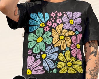 May include: Black t-shirt featuring a colorful floral design with large, smiling daisy-like flowers in shades of blue, green, yellow, pink, and purple. The shirt has the word "BLACK" in a circle on the bottom left.