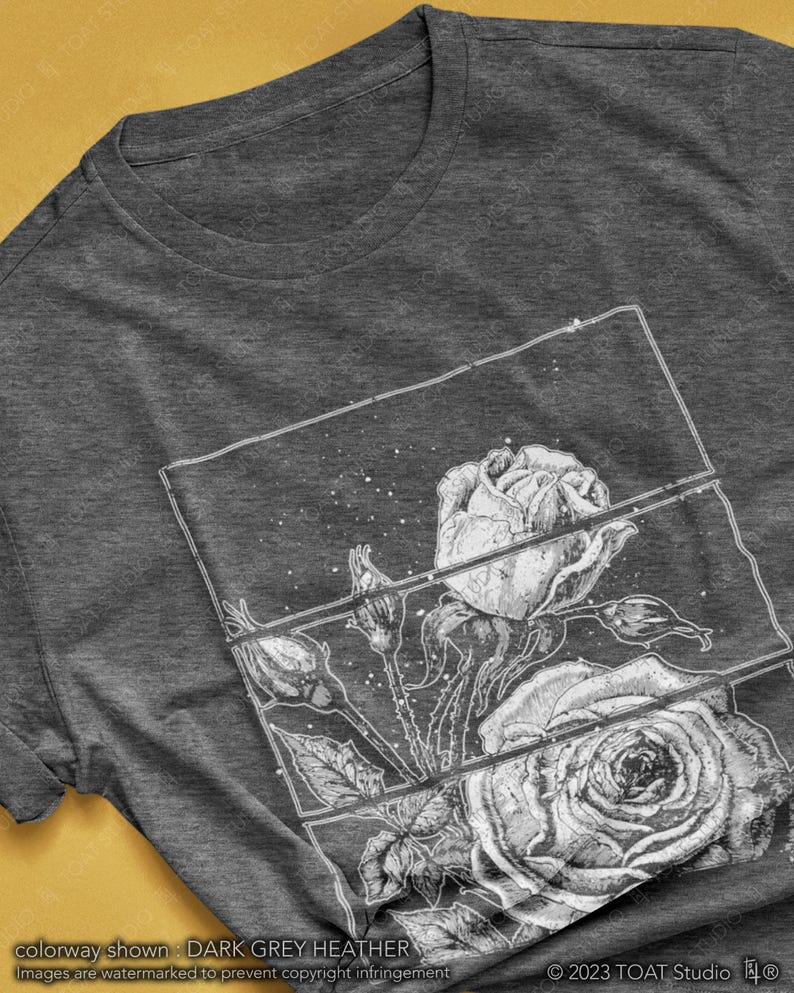 May include: Dark grey heather t-shirt featuring a detailed black and white rose graphic. The design includes a stylized illustration of roses and buds within a rectangular frame. The text "colorway shown: DARK GREY HEATHER" is visible.