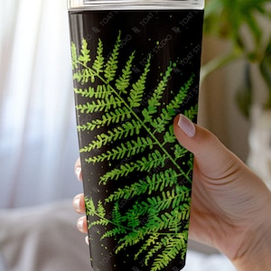 May include: A black and green stainless steel tumbler with a fern leaf pattern. The tumbler has a clear lid.