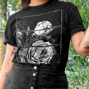 May include: Black t-shirt featuring a detailed black and white rose graphic. The design includes a large rose and smaller buds within a rectangular frame. The text "TOAT STUDIO" is visible on the shirt. The colorway is shown in black.