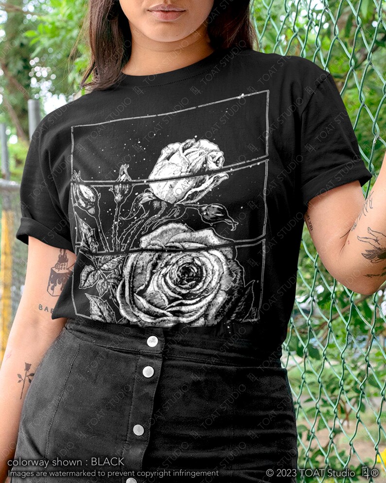 May include: Black t-shirt featuring a detailed black and white rose graphic. The design includes a large rose and smaller buds within a rectangular frame. The text "TOAT STUDIO" is visible on the shirt. The colorway is shown in black.