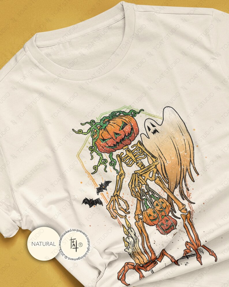 May include: Off-white t-shirt featuring a Halloween-themed graphic. The design includes a skeleton with a pumpkin head, a ghost, bats, and pumpkins. The graphic is in orange, green, and black. The shirt has a round neckline.