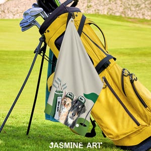 May include: A yellow golf bag with golf clubs and a personalized golf towel featuring two dogs wearing golf hats. The towel has a golf course design with the names "Molly" and "Max" on the hats. The image is set on a green golf course.