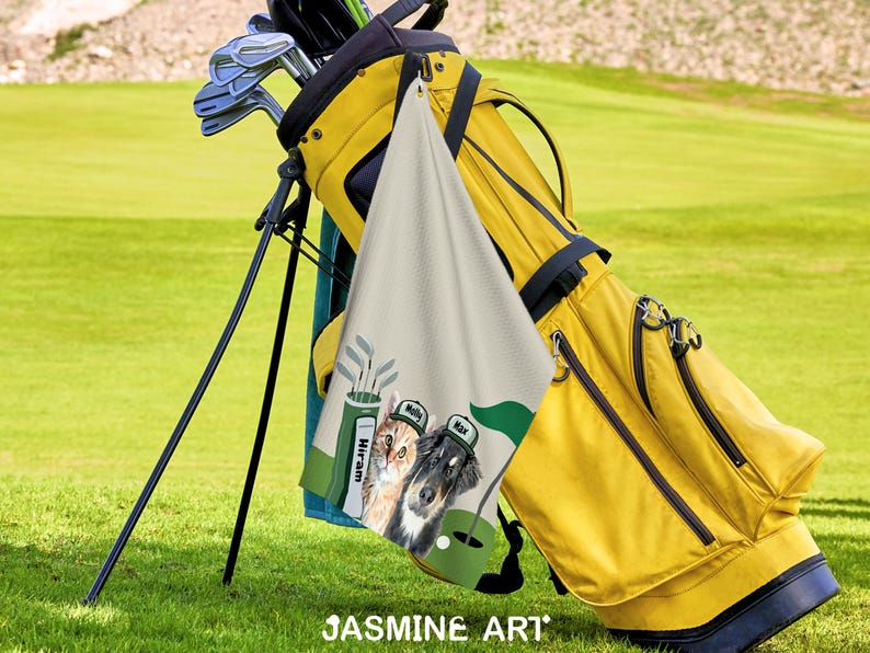May include: A yellow golf bag with golf clubs and a personalized golf towel featuring two dogs wearing golf hats. The towel has a golf course design with the names "Molly" and "Max" on the hats. The image is set on a green golf course.