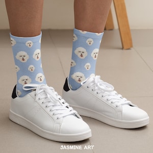 May include: A pair of white sneakers with blue and white socks featuring a repeated pattern of a white dog's face. The socks are crew length and the sneakers have black laces.
