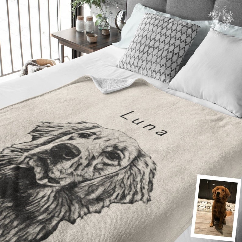May include: A cream-coloured fleece blanket with a black and white illustration of a dog's head. The dog's name, "Luna", is written in black script on the blanket. A smaller photo of the dog is in the bottom right corner of the blanket.